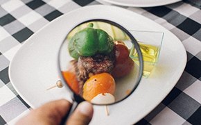 Image shows a plate of food components under a magnifying glass on top of a black and white checkered cloth Image shows a plate of food components under a magnifying glass on top of a black and white checkered cloth