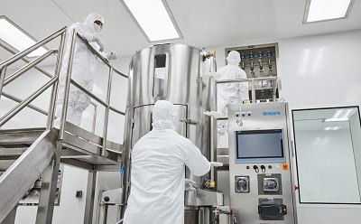 Three individuals in protective suits working with large stainless steel equipment in a clean, well-lit laboratory environment Three individuals in protective suits working with large stainless steel equipment in a clean, well-lit laboratory environment