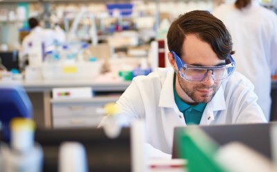 A person in a lab coat working in a well-equipped laboratory. Background includes various laboratory equipment and other individuals A person in a lab coat working in a well-equipped laboratory. Background includes various laboratory equipment and other individuals