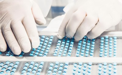 A pair of hands sorting or inspecting blue pills organized in rows on a white tray. A pair of hands sorting or inspecting blue pills organized in rows on a white tray.