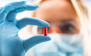 Scientist holding red pill The image depicts a scientist closely examining a pharmacology drug while wearing blue gloves. Their focused attention suggests a laboratory setting, where precision and care are essential.