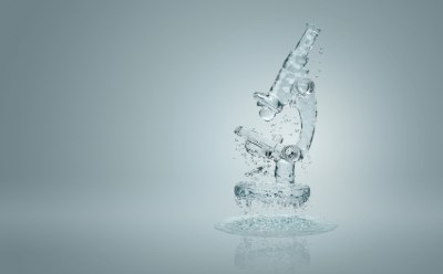 A transparent glass microscope with water droplets suspended in mid-air, set against a light gray background