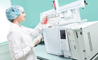 Female scientific researcher with lab coat, gloves and hair protection placing vial flask in gas chromatography instrument Female scientific researcher with lab coat, gloves and hair protection placing vial flask in gas chromatography instrument