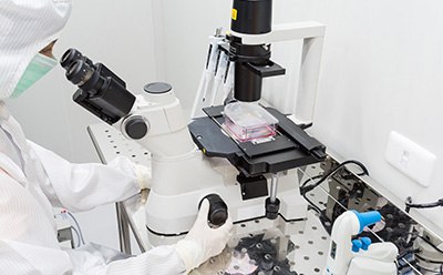Scientist at the microscope Scientist in full protective gown and mask looking through a microscope at cells in a T flask.