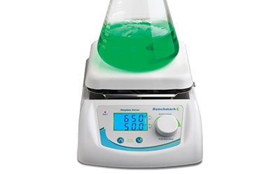 Hotplate Stirrer A digital magnetic hotplate stirrer with a green liquid in a glass beaker placed on top, displaying temperature and speed settings on its screen, with the brand name ‘Heidolph’ and model ‘Hei-Mix L’ visible.