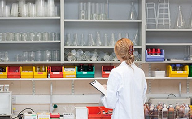 A person in a white lab coat is standing in a laboratory facing away from the camera, holding a clipboard. The laboratory is equipped with shelves stocked with various lab equipment such as beakers, flasks, test tubes, and bottles containing chemicals of different colors. There are also racks of test tubes and other scientific apparatus on the bench in front of the person. The setting suggests a professional research environment, highlighting the meticulous organization and variety of tools used for scientific experiments. A person in a white lab coat is standing in a laboratory facing away from the camera, holding a clipboard. The laboratory is equipped with shelves stocked with various lab equipment such as beakers, flasks, test tubes, and bottles containing chemicals of different colors. There are also racks of test tubes and other scientific apparatus on the bench in front of the person. The setting suggests a professional research environment, highlighting the meticulous organization and variety of tools used for scientific experiments.