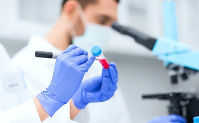 A person in a white lab coat stands in a laboratory facing away from the camera, holding a clipboard and writing notes. The laboratory is equipped with shelves stocked with various lab equipment such as beakers, flasks, test tubes, and bottles containing chemicals labeled with different colors. A person in a white lab coat stands in a laboratory facing away from the camera, holding a clipboard and writing notes. The laboratory is equipped with shelves stocked with various lab equipment such as beakers, flasks, test tubes, and bottles containing chemicals labeled with different colors.
