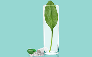 Folates The image depicts a clear glass of water containing a single green leaf, surrounded by scattered pills and capsules. One of the capsules is open, revealing its powder contents.