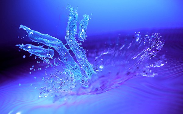 Dynamic splash of water with droplets suspended in the air, illuminated by blue light creating a serene and fluid scene.