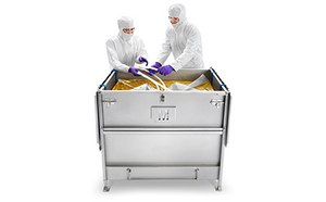 Fluid Management Two people in protective lab attire are interacting with the contents of a large metal container. The container has latches on the side, indicating it may has a lid.