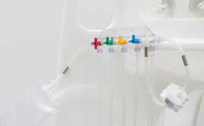 NovaSeptum® SURe sterile sampling assembly connected to a single-use bioreactor A medical manifold with five colored valves: red, yellow, green, blue, and purple. Each valve is connected to transparent tubing, extending from the manifold.
