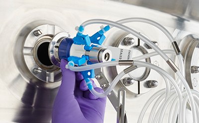 A person is meticulously connecting a blue and white multi-tubing connector to a metallic port on a machine. The individual is wearing a purple glove, emphasizing the need for precision and care in handling the sensitive equipment. The flexible white tubes extend out of the frame, suggesting their connection to a larger system. A person is meticulously connecting a blue and white multi-tubing connector to a metallic port on a machine. The individual is wearing a purple glove, emphasizing the need for precision and care in handling the sensitive equipment. The flexible white tubes extend out of the frame, suggesting their connection to a larger system.