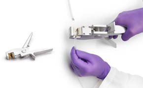 Add a Crimper for Aseptic Disconnection A person wearing purple gloves handling a scientific instrument, with another similar instrument lying nearby on a white surface.