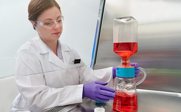 A woman in a white lab coat, working with laboratory flask containing a red liquid, which is connected to another piece of equipment with blue liquid at the bottom.  A woman in a white lab coat, working with laboratory flask containing a red liquid, which is connected to another piece of equipment with blue liquid at the bottom.