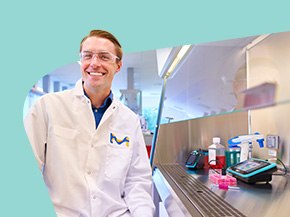 Scientist in a white lab coat with the Merck KGaA, Darmstadt, Germany “M” logo beside a biosafety cabinet containing cell culture tools—pipette controller, media bottle, and culture dishes with pink medium—against a teal graphic background.