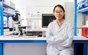 Target Discovery Scientist standing and holding a box of MILLIPLEX® multiplexing biomarker assay reagents next to a Luminex® instrument with an SMCxPRO® ultrasensitive immunoassay instrument on a bench in the background