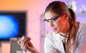 Amino Acid, Peptide & Protein Standards Brown-haired female scientist wearing white lab coat and safety goggles writes a chemical structure on glass screen. Computer screen and lab setting are visible in background.