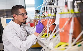 Contract Services A man wearing safety glasses operating a 3-liter single-use bioreactor in a laboratory filled with multiple 3 liter single-use bioreactors.