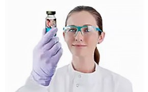 Sterile Drug Product  A female scientist wearing protective goggles holds up a sterile drug product.