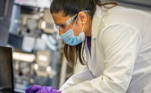 Data Entry Scientist Researcher enters data in a computer in a lab setting, wearing glasses, mask, gloves and a lab coat