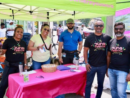 A group of employees stand together at a community event. They are standing under a company tent and smiling at the camera.  A group of employees stand together at a community event. They are standing under a company tent and smiling at the camera.