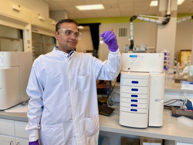 Mahesh lab Karwa stands in lab next to an analytical instrument that helps determine the purity of mRNA.
