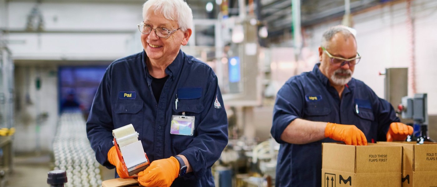 packaging line Two employees wear uniforms, gloves and safety glasses and package boxes.