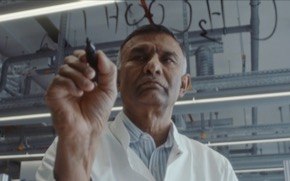 ponnusamy-green-chemistry Dr. Ponnusamy wears a lab coat is writes out chemical compounds on glass with a marker.