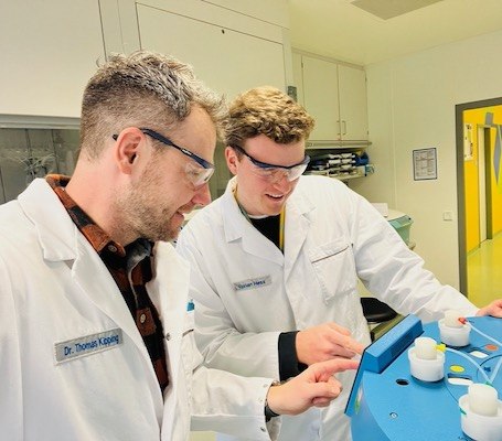 Thomas Kipping and Florian Hess work together on an instrument. They both wear safety glasses and look at the control panel .