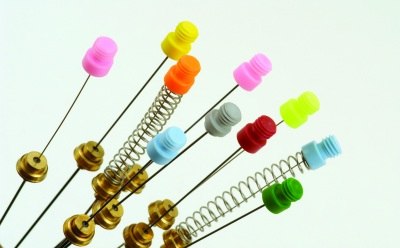 Nitinol-core SPME fiber The image appears to be a collection of metallic colorful push pins and springs. The pin heads are of plastic and contain pink, green, yellow and other colors.