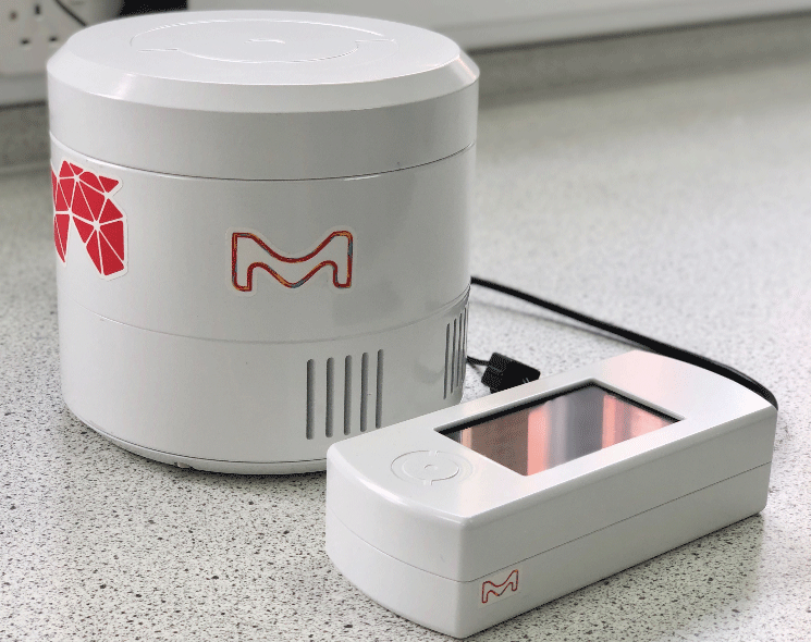 LightOX Photoreact 365  A close-up view of the LightOX Photoreact 365, featuring a round white photoreactor unit with the M logo in red, alongside a rectangular control device with a digital display. The devices are placed on a light-colored laboratory countertop, with a power cable connecting them.