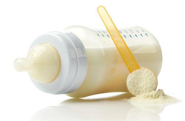 Infant formula A baby bottle filled with milk, accompanied by a yellow measuring scoop and powdered formula on a white surface