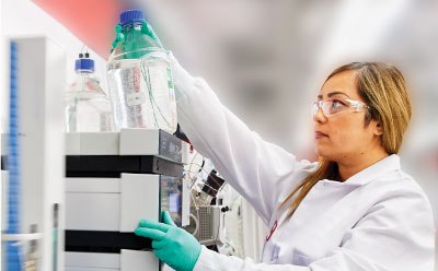 Female researcher in lab coat and gloves operating an HPLC during analysis of oligos Female researcher in lab coat and gloves operating an HPLC during analysis of oligos