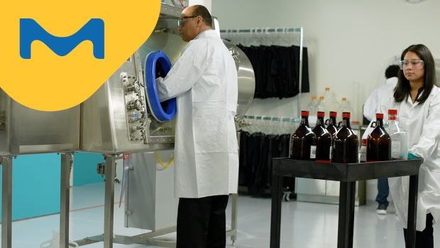 <p>The Secret of HPAPI Production Success</p>
 A male scientist in a lab coat is using an isolator, while a colleague female scientist in a lab coat is transferring chemicals into the training facility behind him.